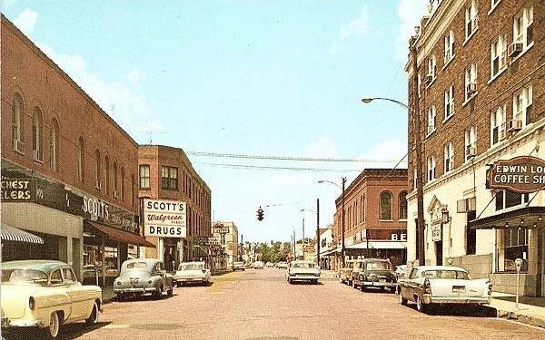 Vintage color postcard of Pine Street showing classic storefronts and cars from mid-century Arkansas