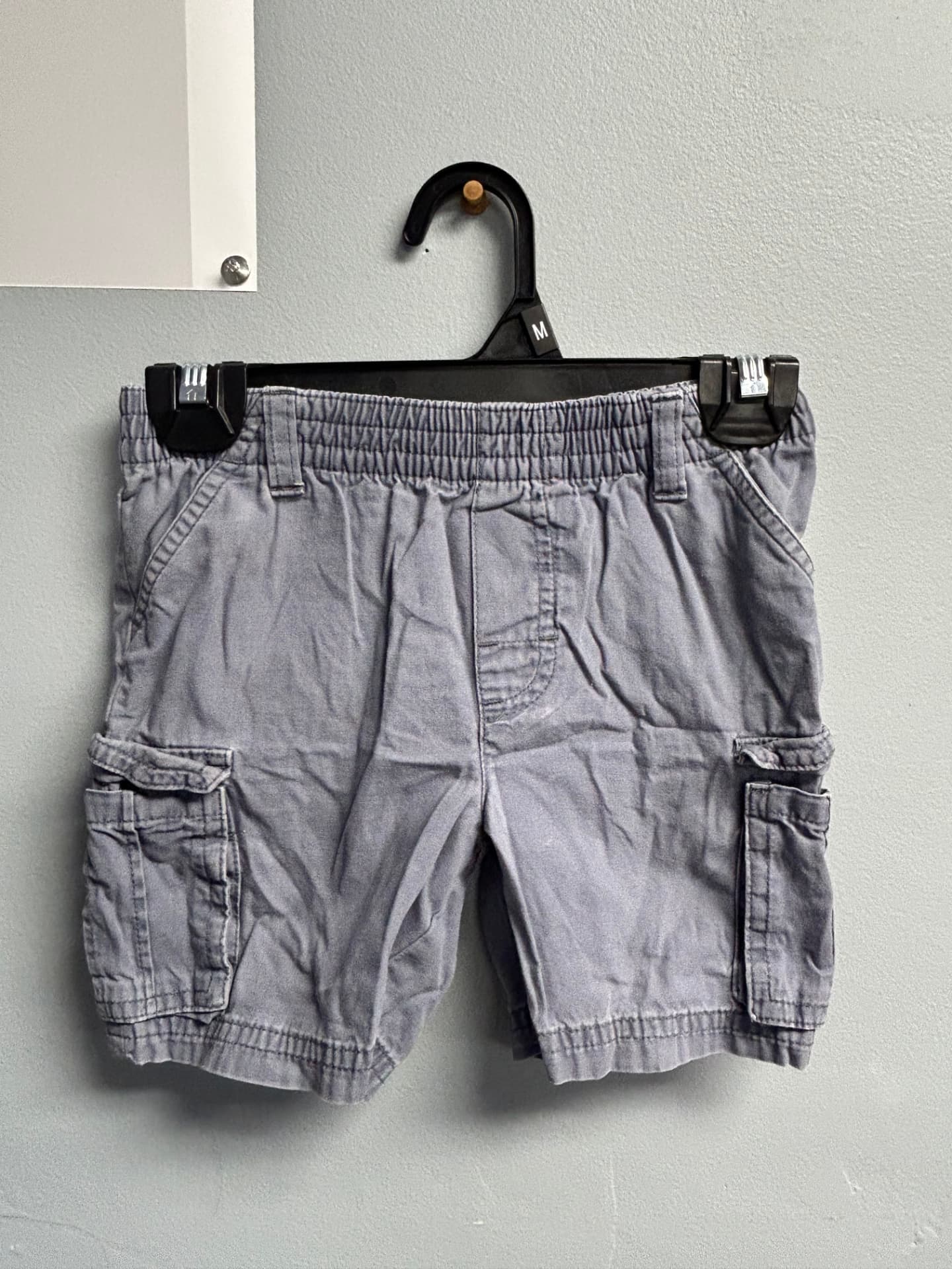 Light grey cargo shorts with elasticated waist and side pockets on a hanger