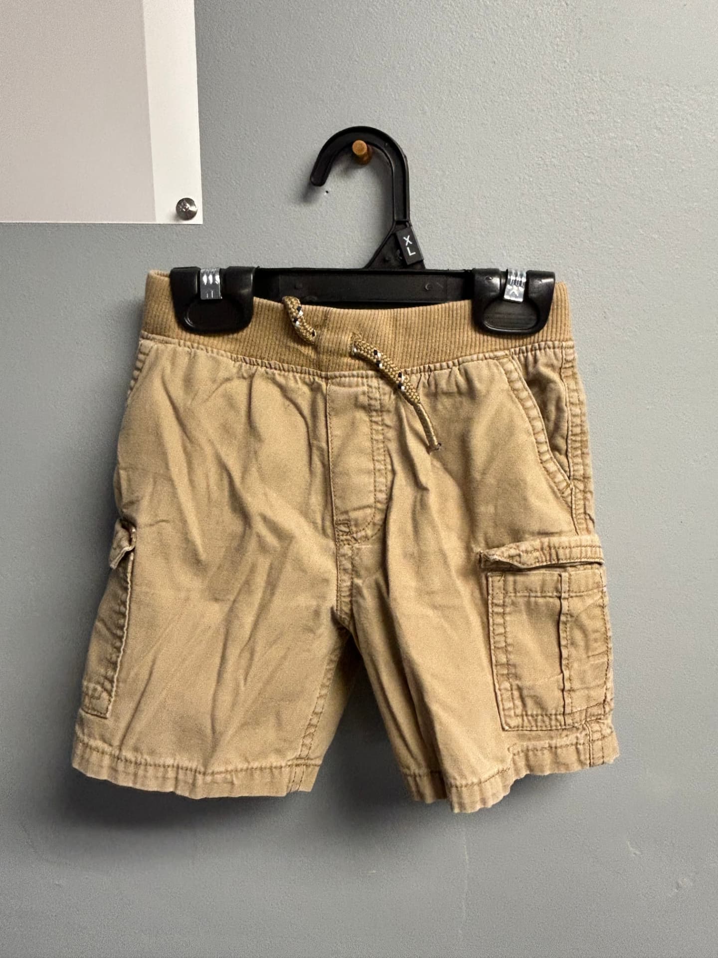 Tan cargo shorts with a patterned drawstring waist on a hanger