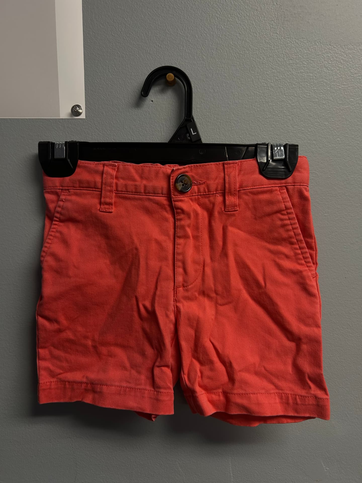 Bright coral chino-style shorts with belt loops on a hanger